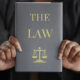 Hands, woman or judge with book called "The Law"